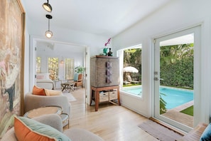 A spacious living area with a pool view, a large painting, and a wooden cabinet with decorative items.