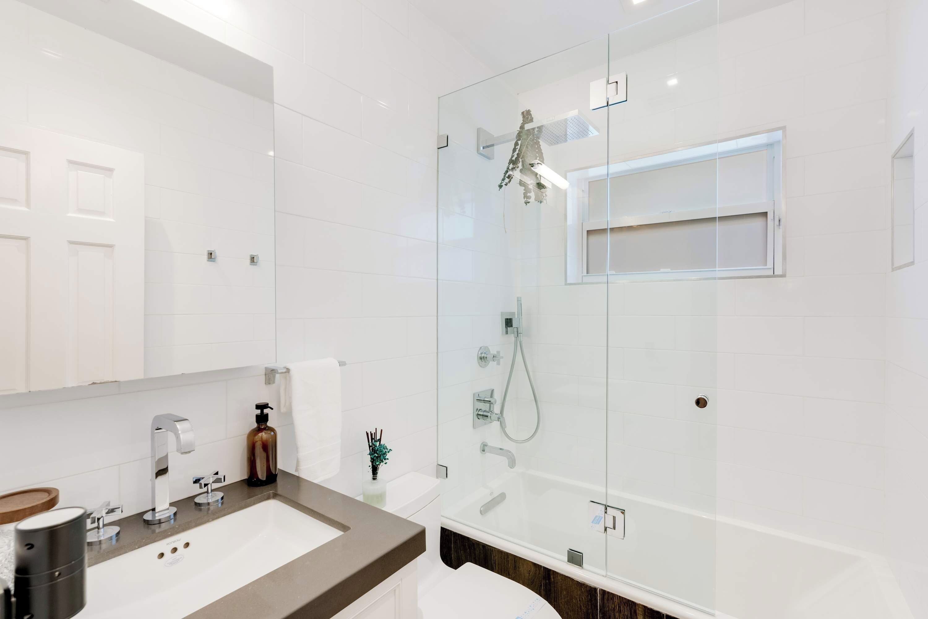 A modern bathroom with a glass-enclosed shower, a white sink, and a large mirror.