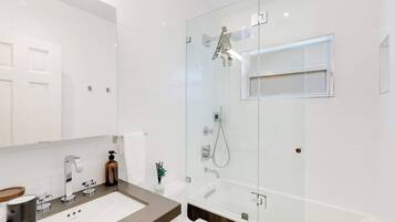A modern bathroom with a glass-enclosed shower, a white sink, and a large mirror.