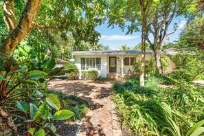 A house with a brick pathway leading to the front door, surrounded by lush greenery and trees. - Garden Grove, 3BR Miami Home With Private Pool (Miami)
