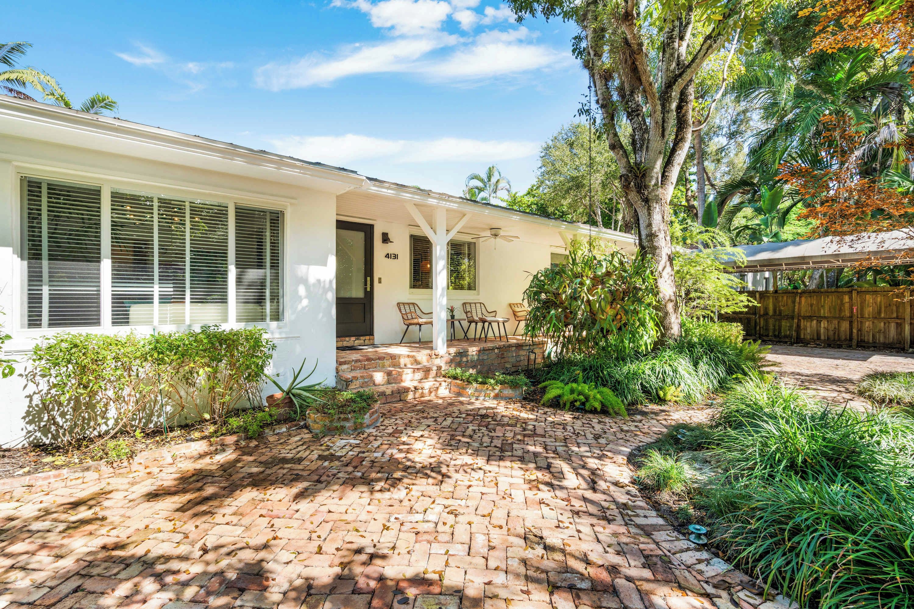 A white house with a brick patio, a covered porch, and a wooden fence.
