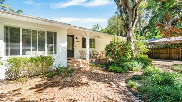A white house with a brick patio, a covered porch, and a wooden fence.