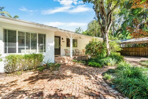 A white house with a brick patio, a covered porch, and a wooden fence. - Garden Grove, 3BR Miami Home With Private Pool (Miami)