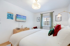 A bedroom with a bed, a TV, a bedside table, a lamp, and a window with curtains. - Garden Grove, 3BR Miami Home With Private Pool (Miami)