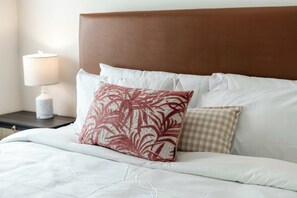 Una cama bien hecha con cabecera marrón, ropa de cama blanca y almohadas estampadas.