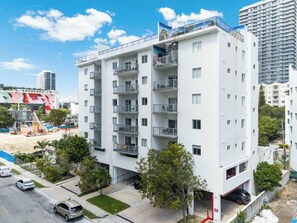 Un edificio residencial de varios pisos con balcones, un estacionamiento y una zona de construcción al fondo.