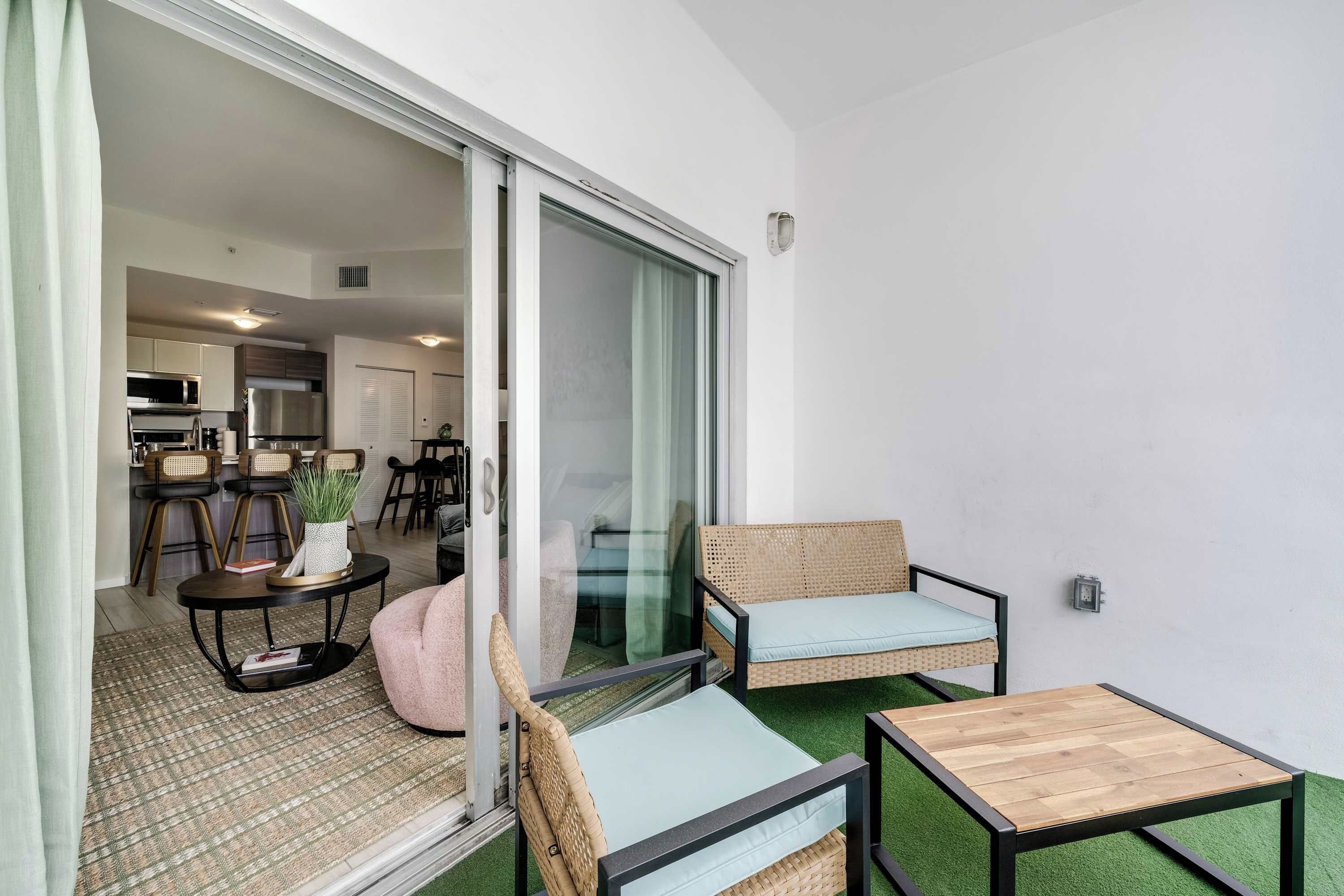 Uma sala de estar moderna com uma porta de vidro deslizante que dá para uma cozinha, uma pequena mesa de madeira e dois sofás de vime.