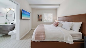 A bedroom with a bed, a bedside table, a nightstand, a window with blinds, and a bathroom with a toilet and sink. - Edgewater Pad- Balcony, Parking and Prime Location (Miami)