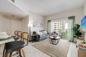 Una sala de estar con un sofá, sillas, una mesa de centro, una mesa de comedor con sillas y vistas al exterior.