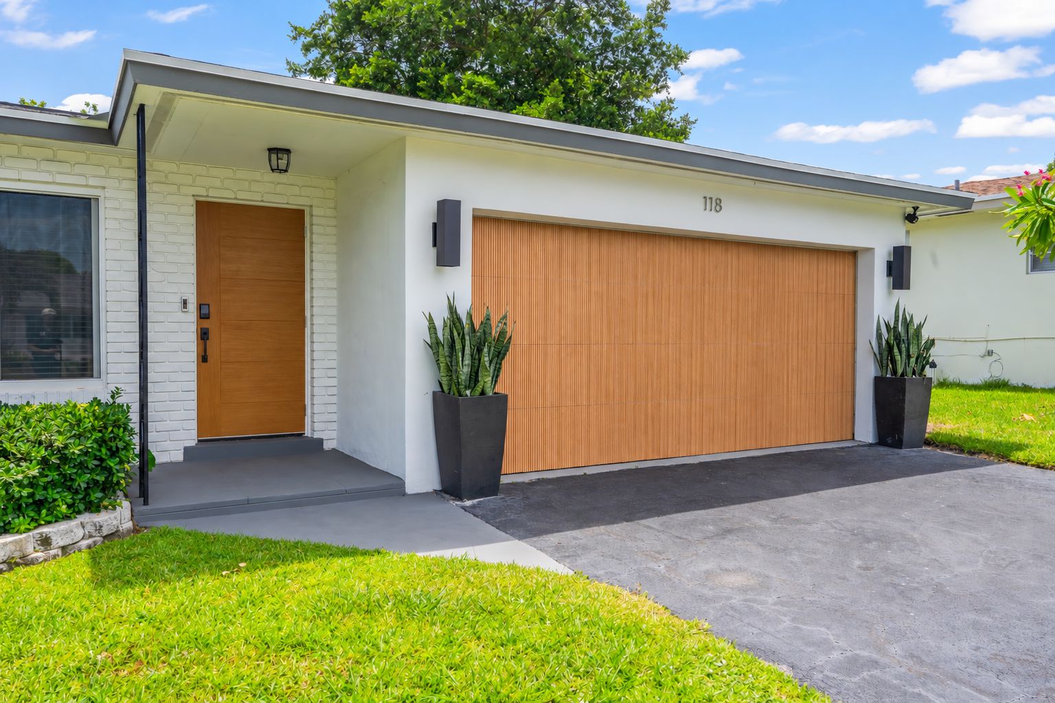 A modern two-story house with a garage, a front door, and two potted plants.