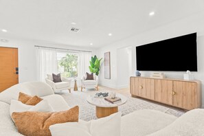 Ein modernes Wohnzimmer mit einer Couch, Sesseln, einem Couchtisch, einem Fernseher und einem Schrank.