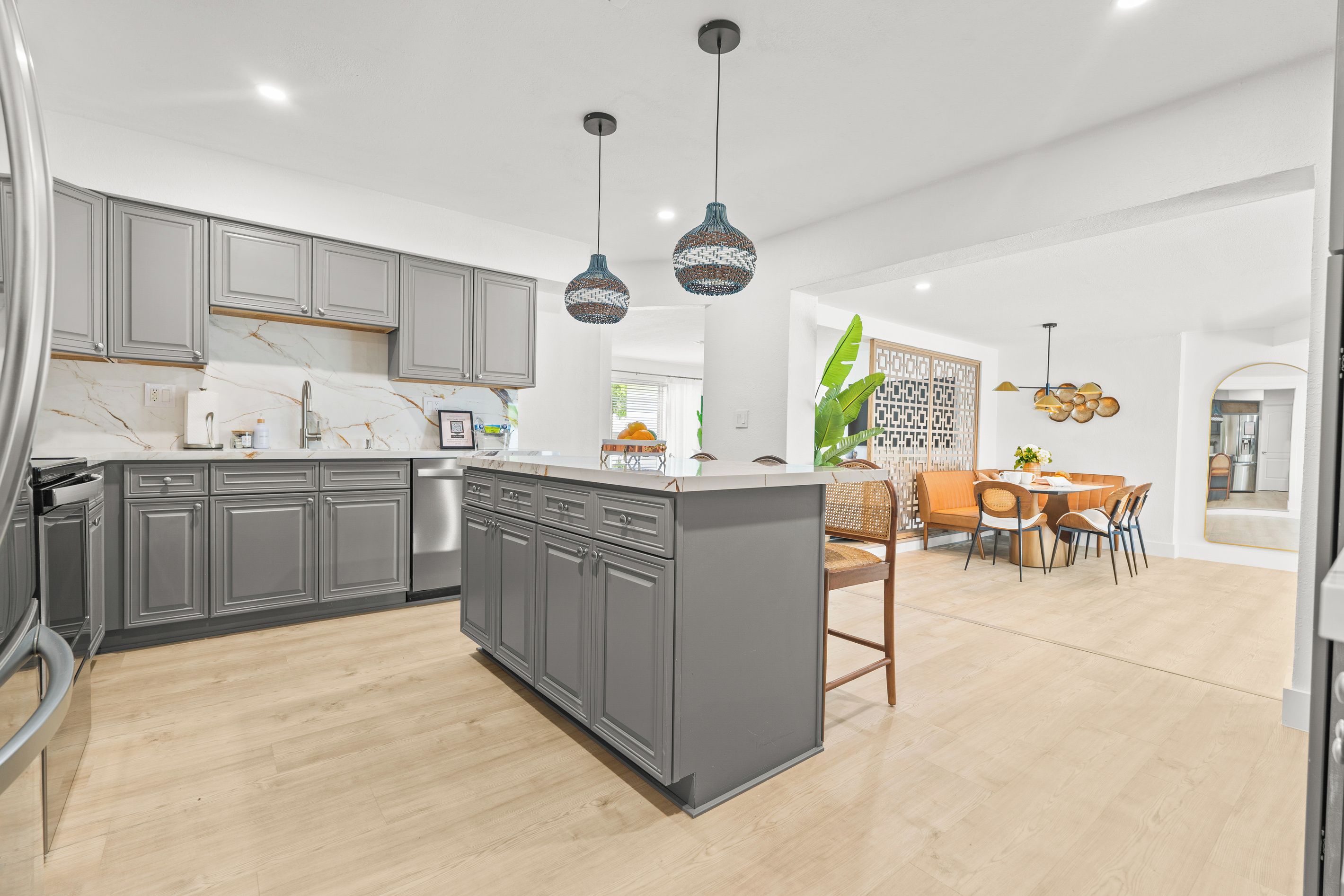 A modern kitchen with grey cabinets, a marble countertop, and pendant lighting.