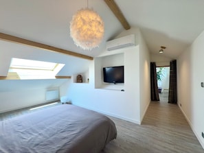 Ein Schlafzimmer mit einem Bett, einem an der Wand befestigten Fernseher und einem Oberlicht.