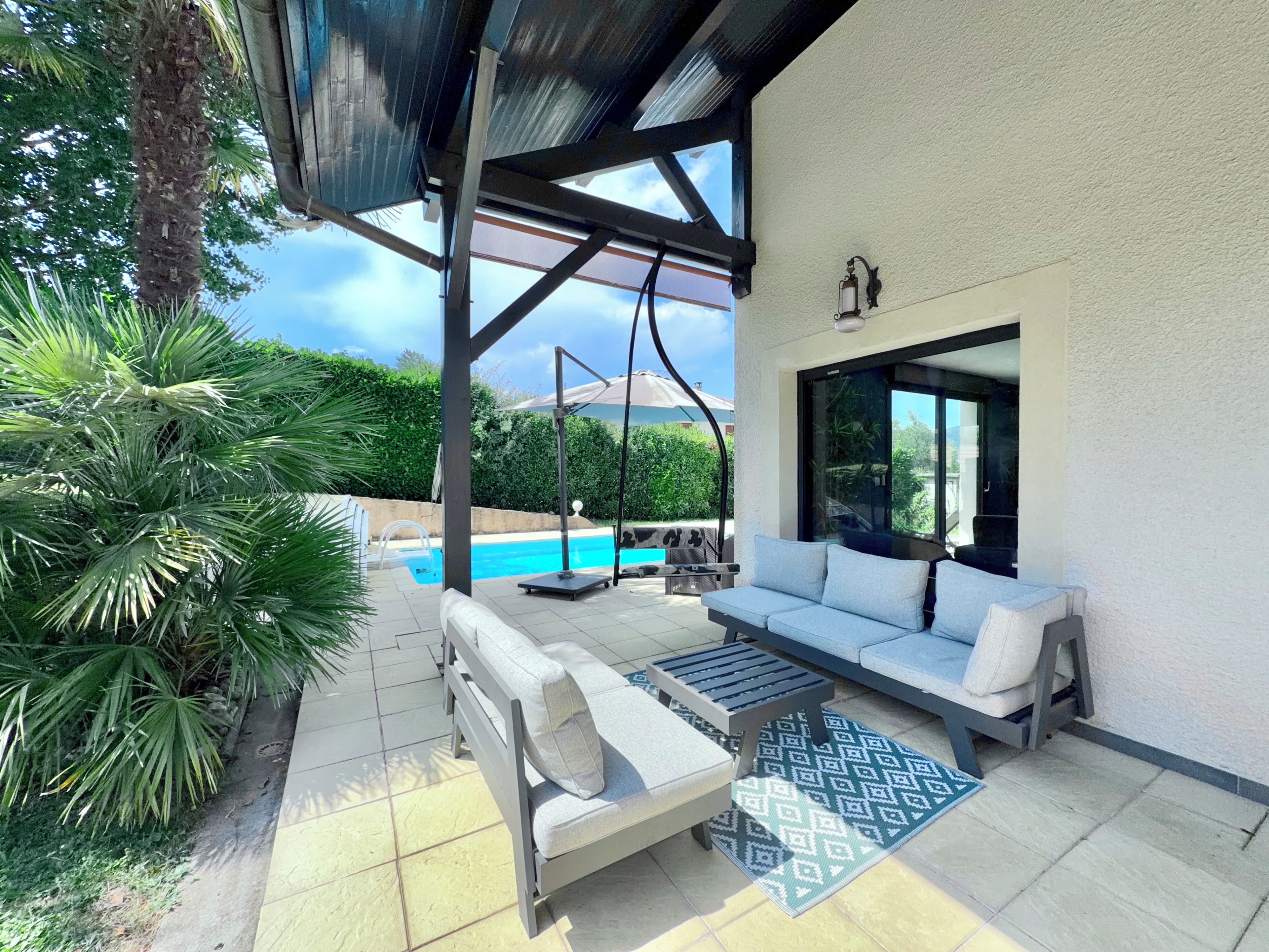 Un espacio de estar al aire libre techado, con piscina, sofá y mesa.
