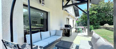 A covered outdoor seating area with a sofa, a table, and a grill.