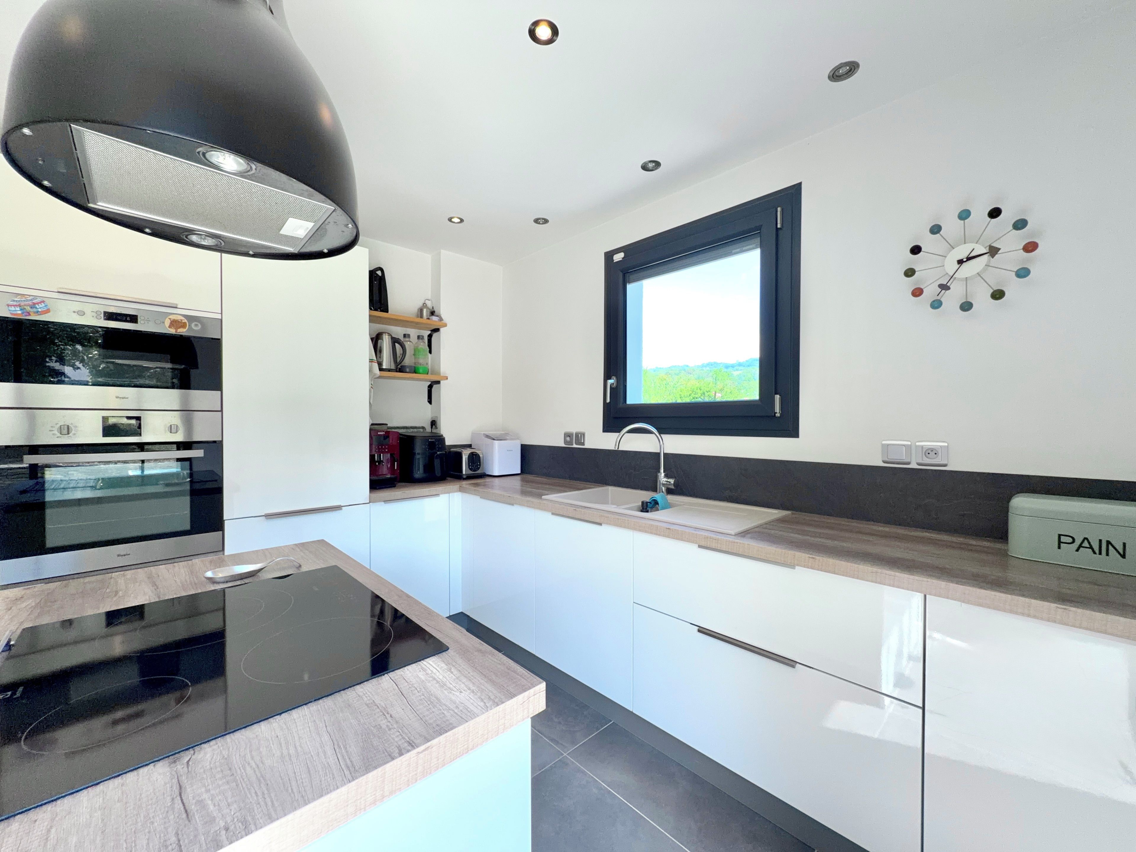 A modern kitchen with built-in appliances, a window, and a wall clock.