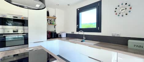 A modern kitchen with built-in appliances, a window, and a wall clock.