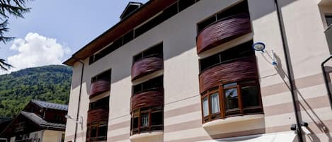 A multi-story hotel with balconies, a mountain backdrop, and a clear sky.