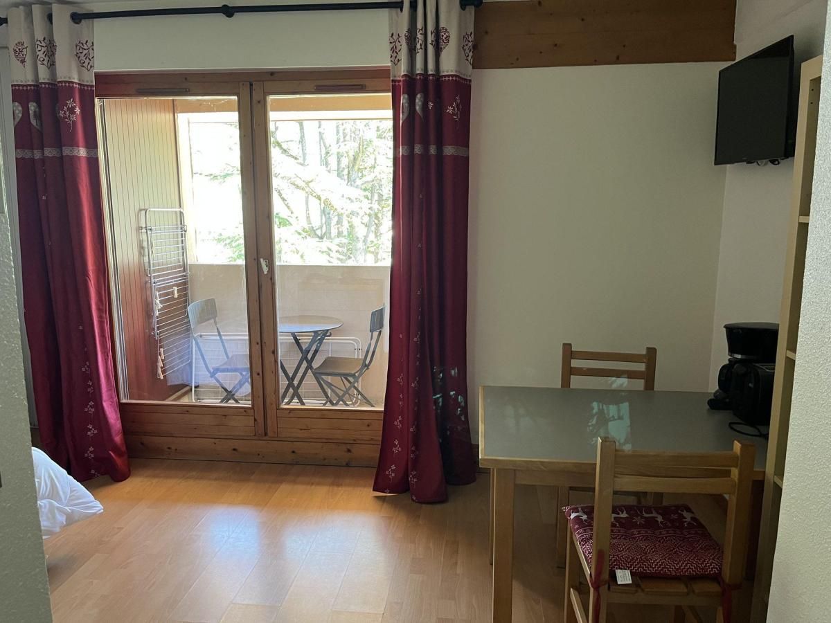 A room with a wooden floor, a glass table, and a chair. There is a sliding glass door leading to an outdoor area with a chair and a table.