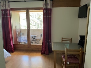 A room with a wooden floor, a glass table, and a chair. There is a sliding glass door leading to an outdoor area with a chair and a table. - 200m from ski lifts, 4th floor, balcony, tv, 23m², Brides Les Bains (Brides-les-Bains)