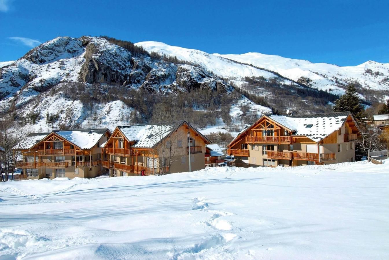 En rad med trähus med balkonger, med snötäckta berg och en klarblå himmel som bakgrund.