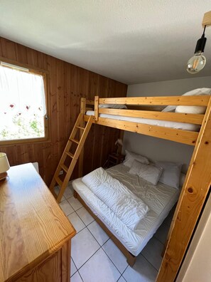 Ein Etagenbett mit Holzleiter, ein Nachttisch und ein Fenster mit Vorhängen.