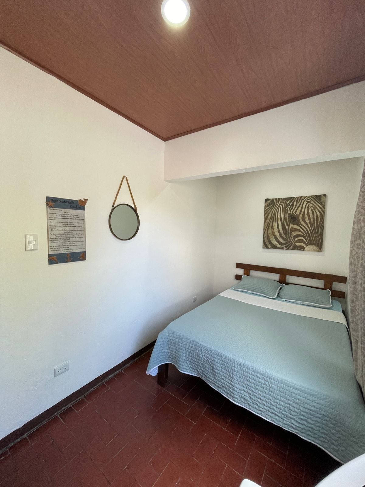 Un dormitorio con una cama, un espejo fijado a la pared, una obra de arte con estampado de cebra y una lámpara en el techo.