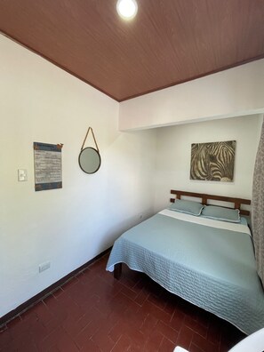 Een slaapkamer met een bed, een spiegel aan de muur, een kunstwerk met een zebra patroon en een plafondlamp.