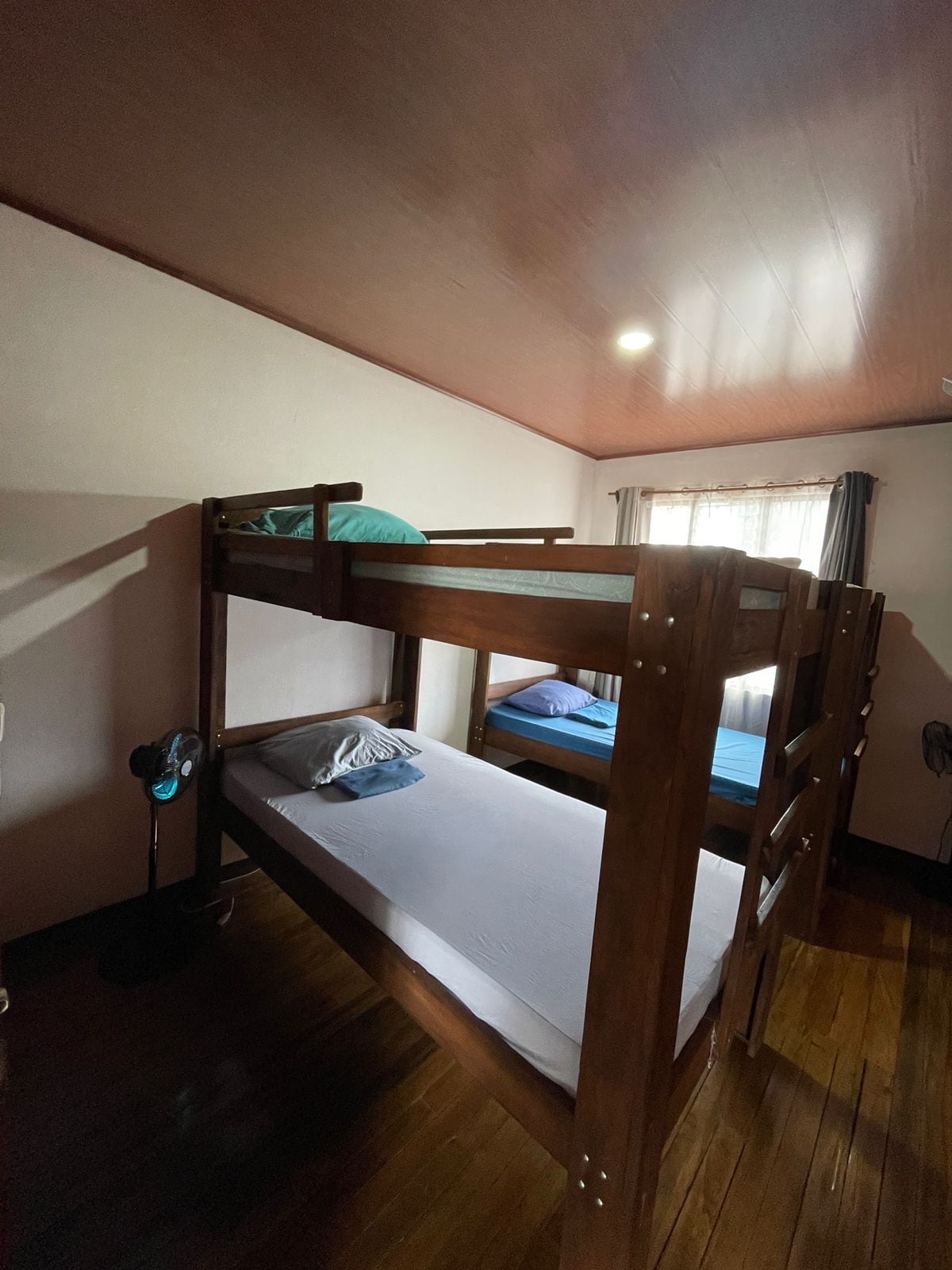 Quarto com beliche, ventilador de teto e janela com cortinas.