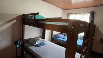 Quarto com beliche, ventilador de teto e janela com cortinas.