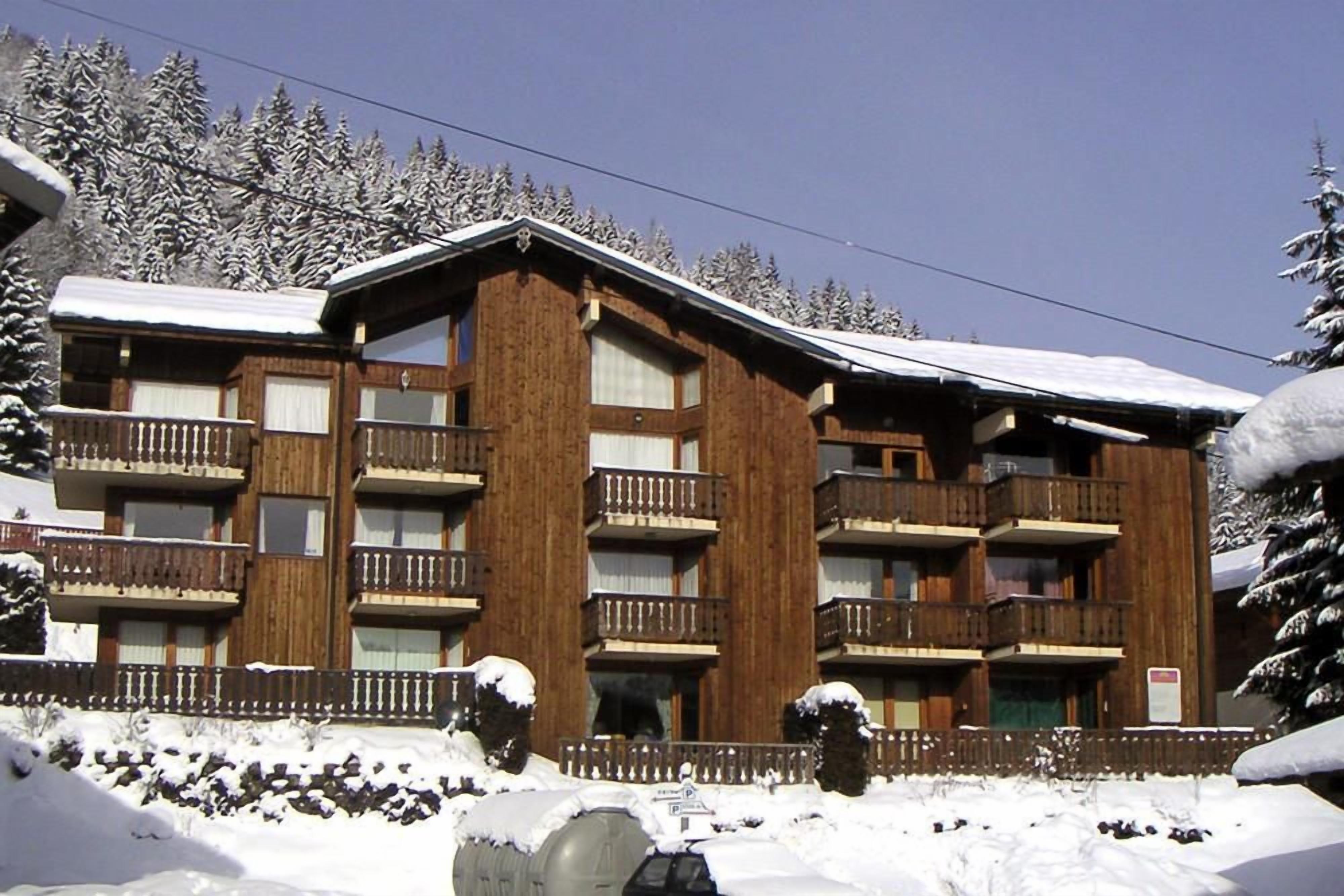 A multi-story wooden building with balconies, surrounded by snow-covered trees.