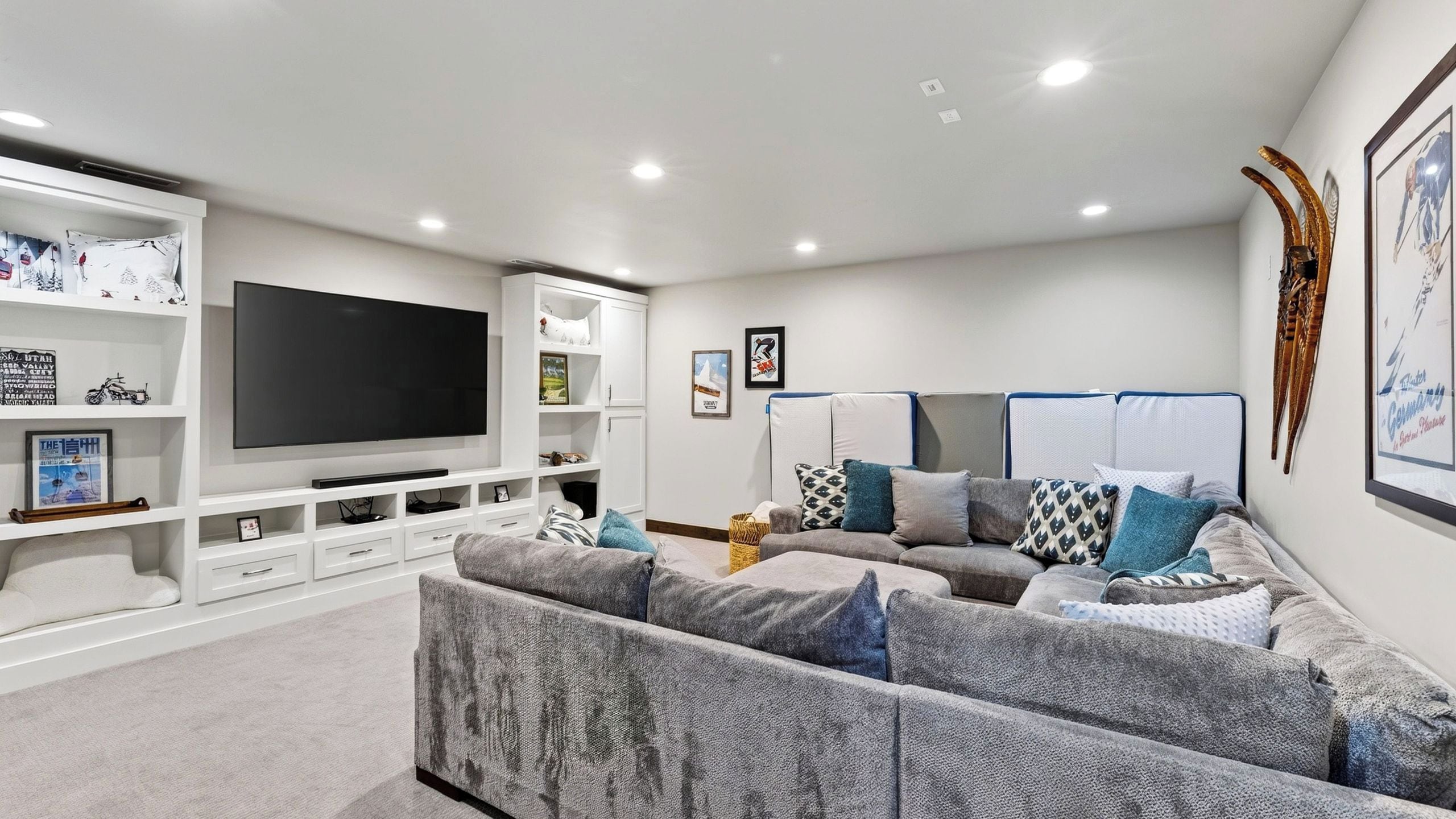 Una sala moderna con un televisor de pantalla plana grande, un sofá modular gris y un mueble de entretenimiento blanco.
