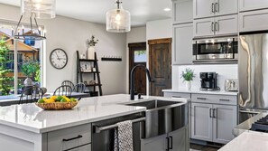 A modern kitchen with stainless steel appliances, a large island with a bowl of fruit, and a clock on the wall. - High West Hideaway by Avantstay Mountain-view Townhome Hot Tub + Firepit Near Park City (Heber City)