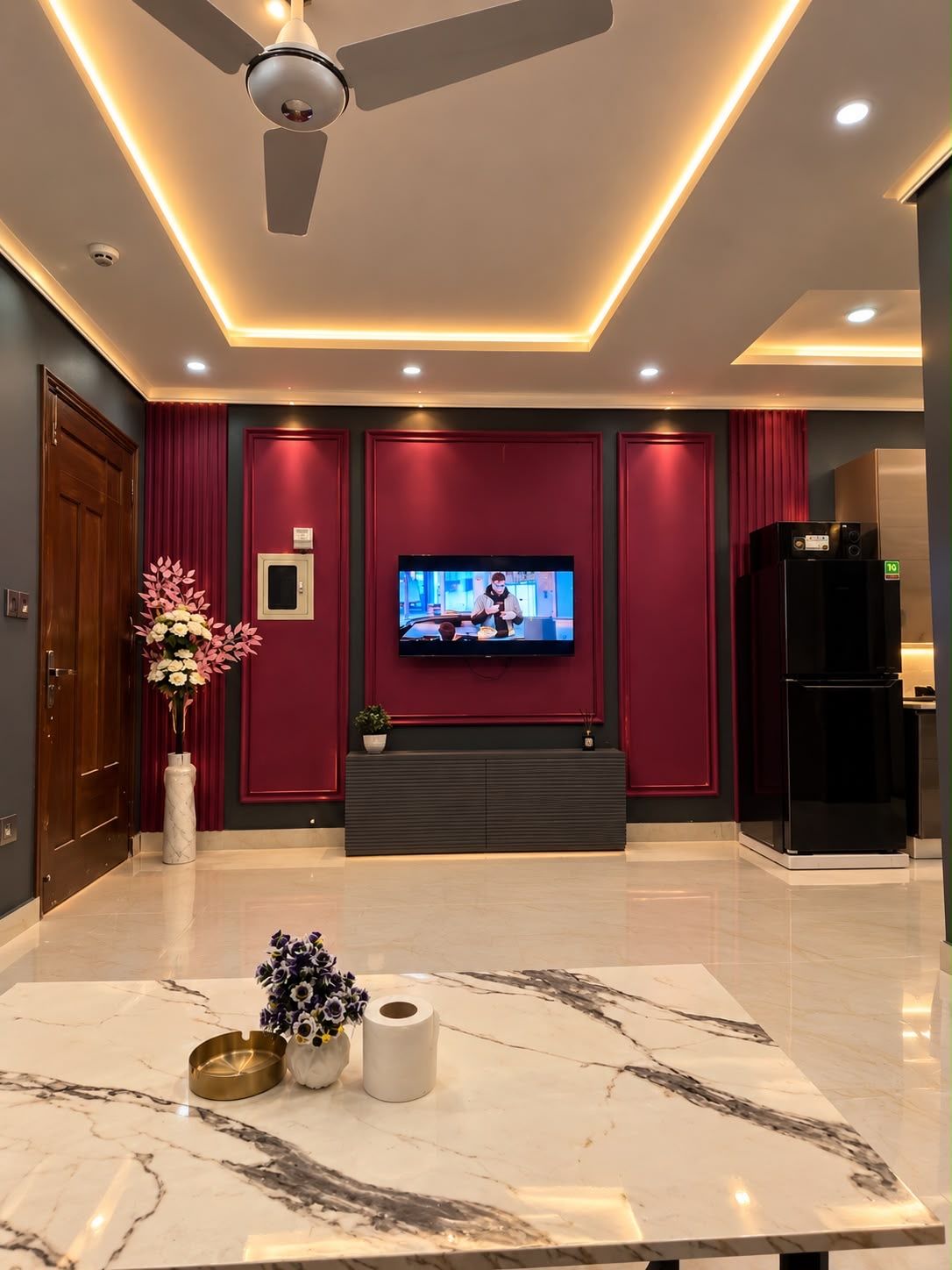 A modern living room with a flat-screen TV, a ceiling fan, and a marble coffee table.