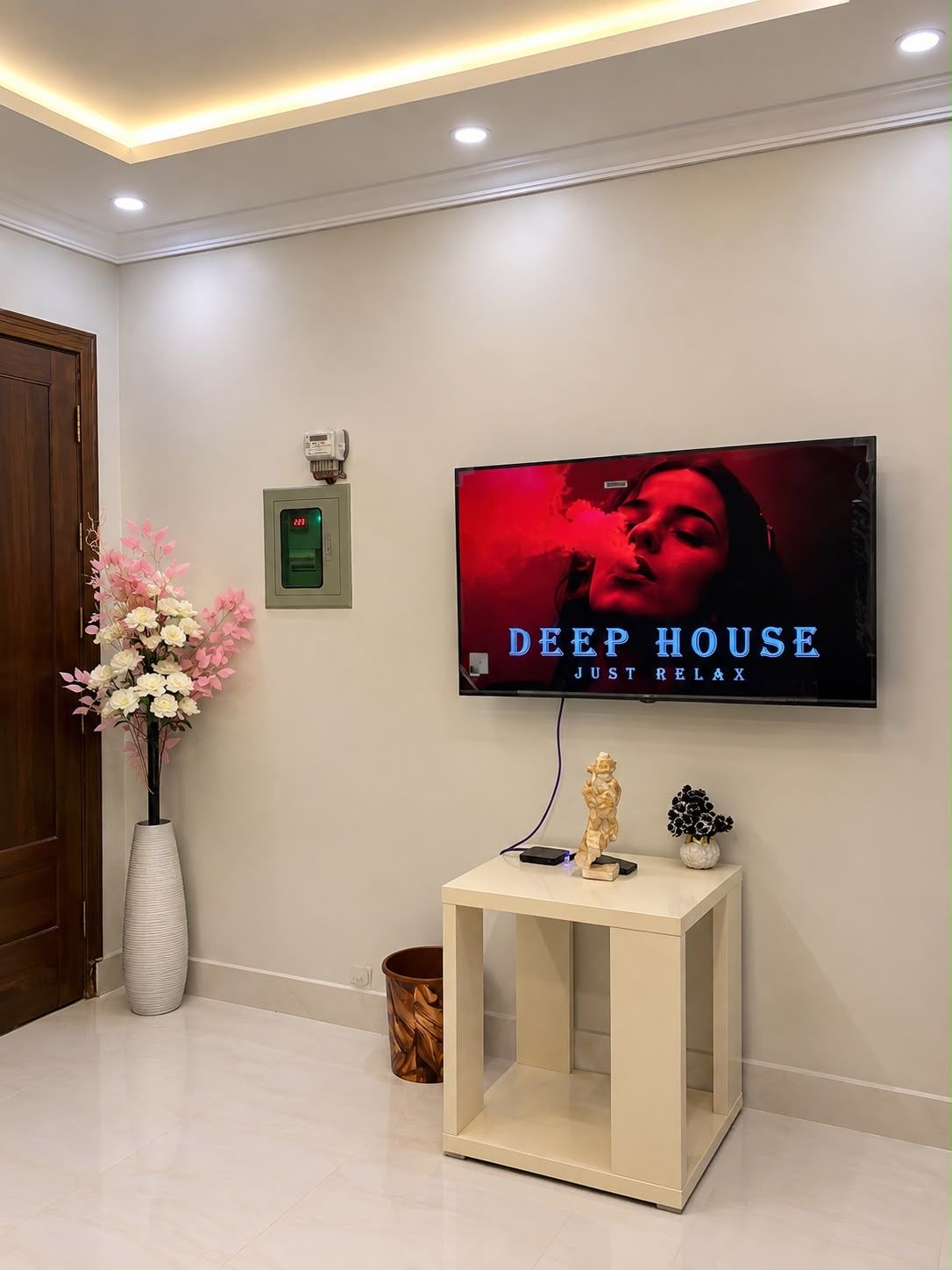 A modern interior with a flat-screen TV mounted on the wall displaying 'DEEP HOUSE JUST RELAX'.