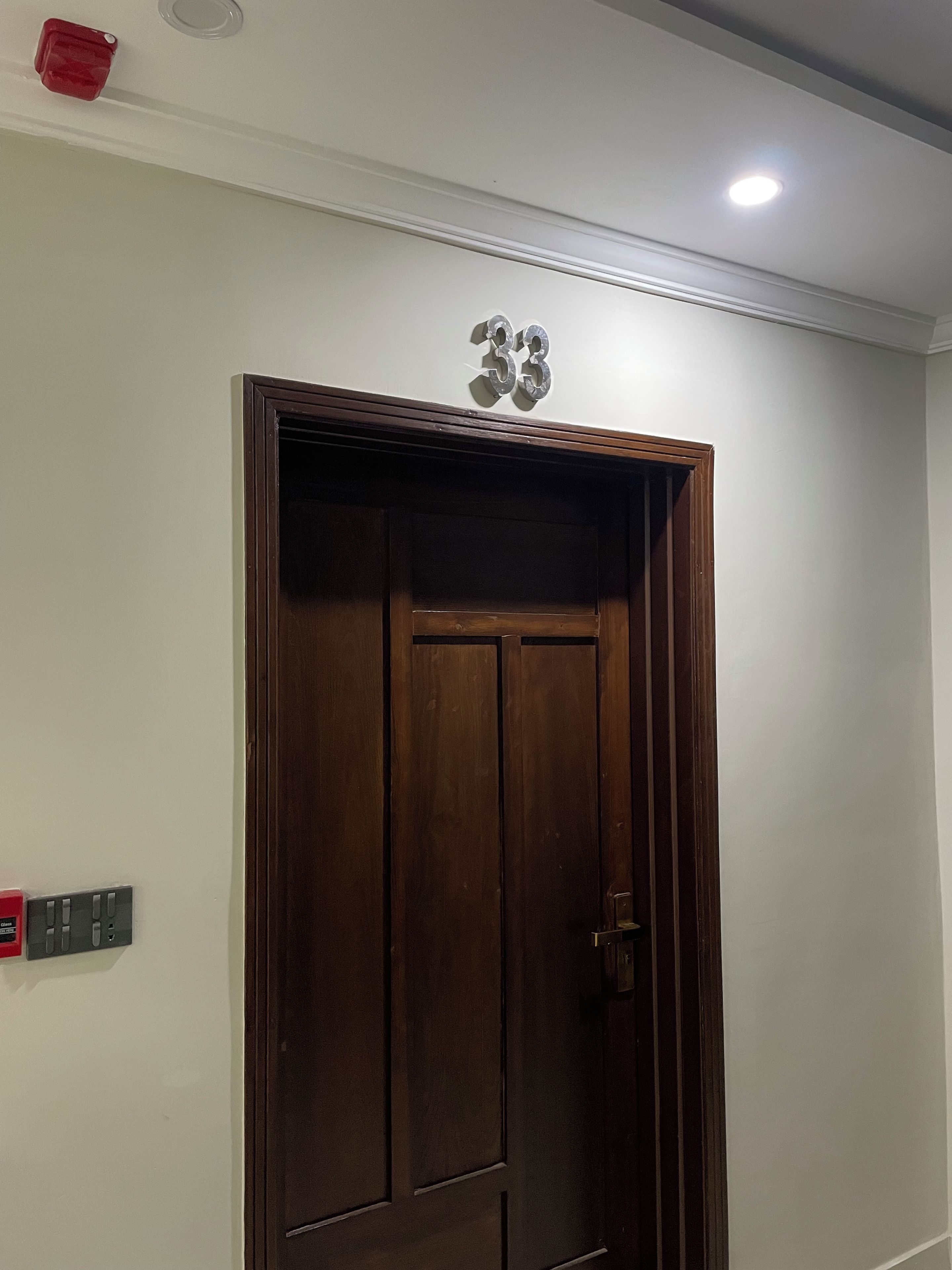 A wooden door with a number '53' above it, a light fixture on the ceiling, and a wall-mounted electrical outlet to the left.