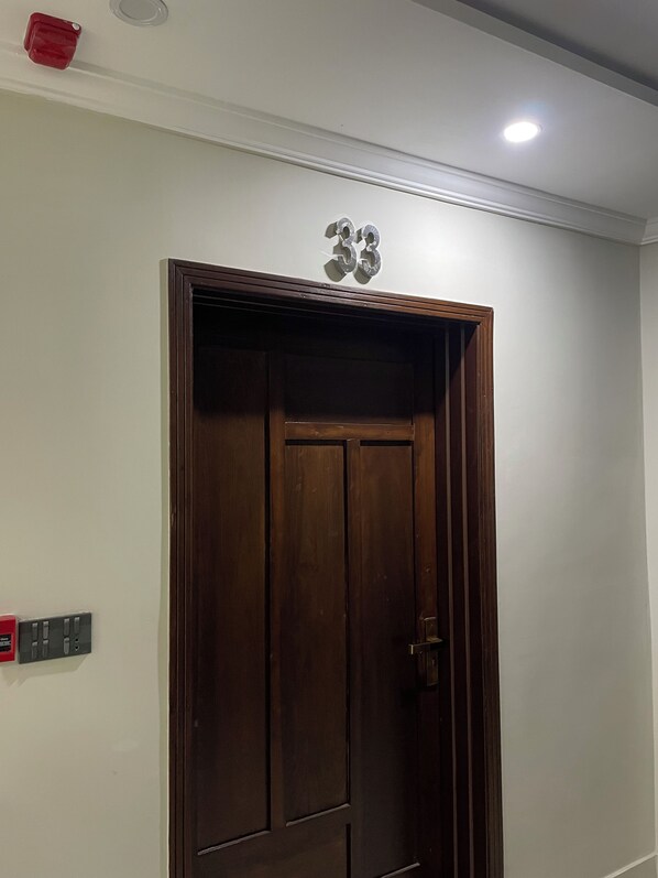Una puerta de madera con el número '53' encima, un accesorio de iluminación en el techo y un enchufe en la pared a la izquierda.