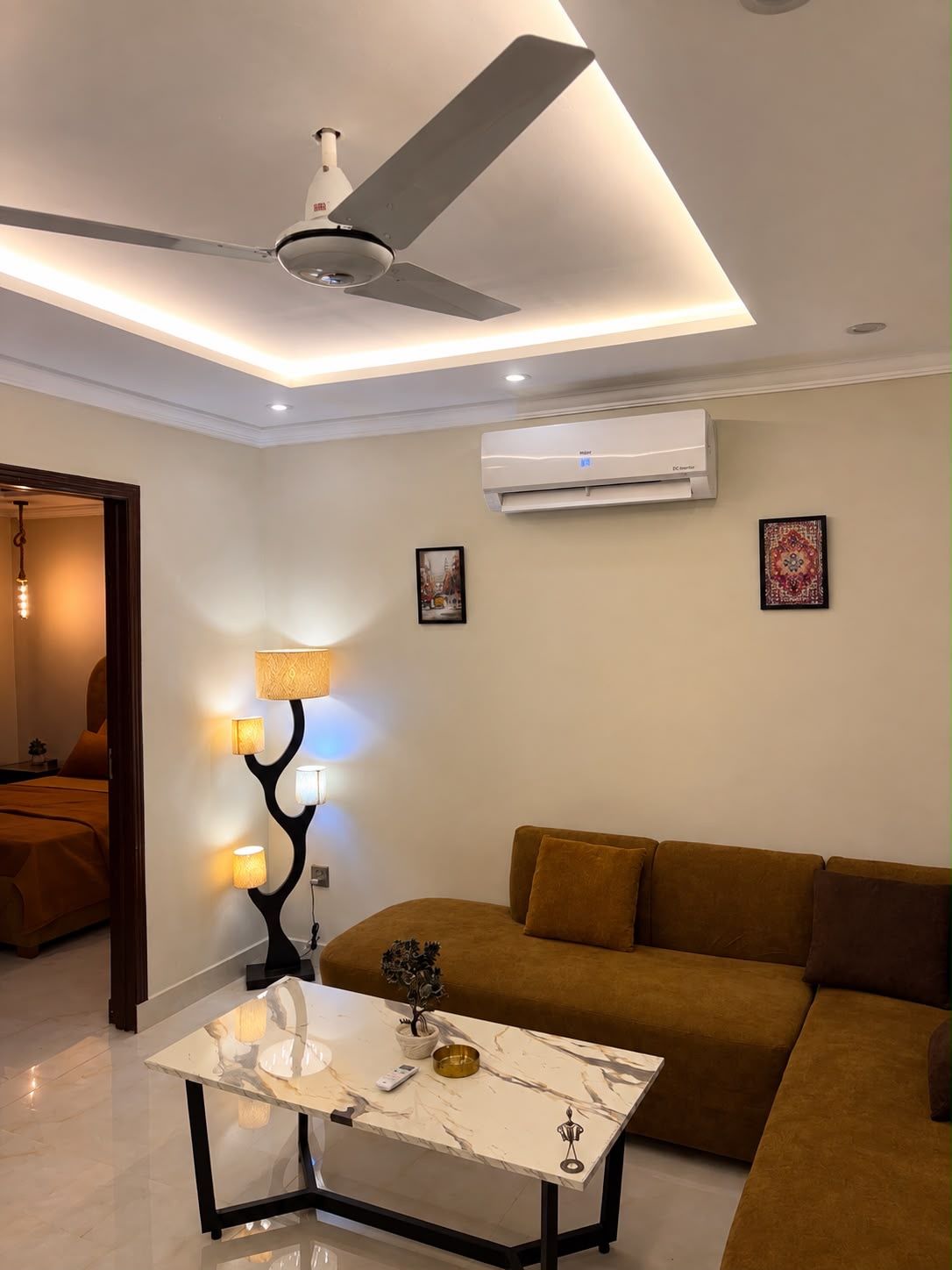 Un salon moderne doté d’un ventilateur de plafond, d’une table basse en marbre, d’un canapé et d’un climatiseur fixé au mur.