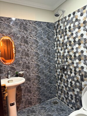 A bathroom with a marble sink, a mirror, a shower with a hexagonal tile pattern, and a toilet. - Cozy 1-bedroom apartment in pleasant Lahore with AC comfort (Lahore)
