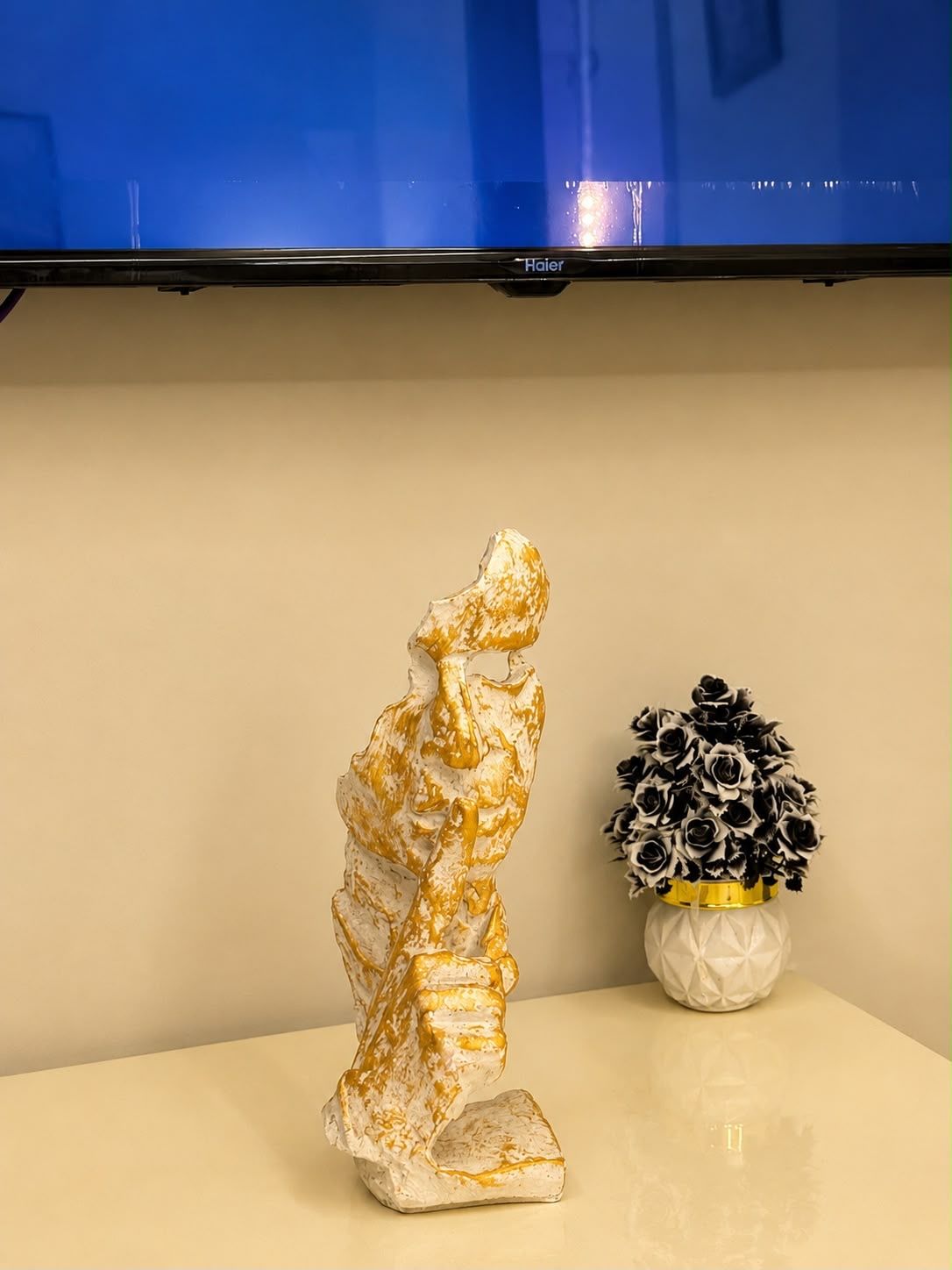 A sculpture of a figure in a dynamic pose, a vase with black and white flowers, and a flat-screen television mounted on a wall.