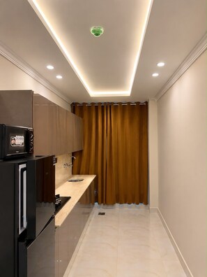 A compact kitchen with a built-in refrigerator, a microwave, and a sink. - Cozy 1-bedroom apartment in pleasant Lahore with AC comfort (Lahore)