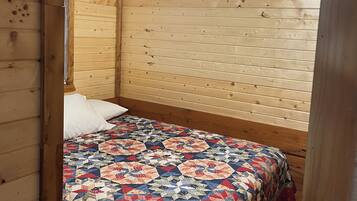 A cozy bedroom with a wooden ceiling and sloped roof, featuring a bed with a colorful quilt and a ceiling fan.