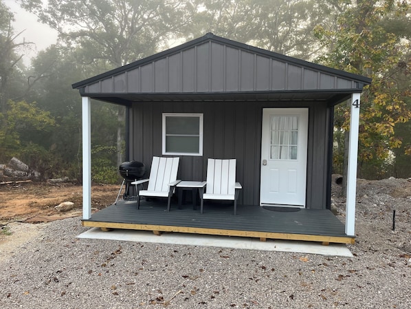 Eine kleine, dunkel gefärbte Holzhütte mit Veranda, zwei Adirondack-Stühlen und einem Grill.