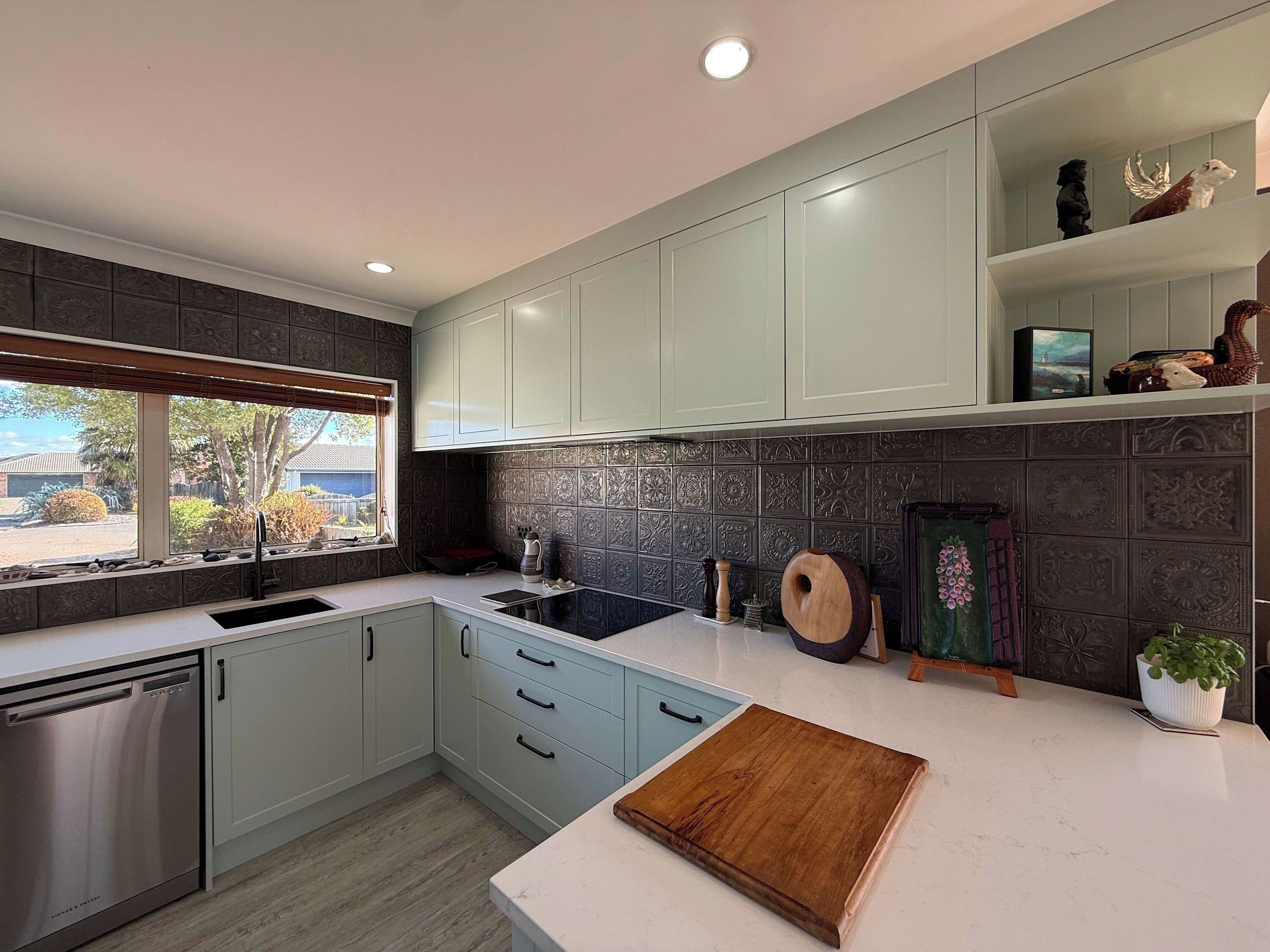 A modern kitchen with light blue cabinets, a stainless steel dishwasher, a black stove, and a wooden cutting board on the countertop.