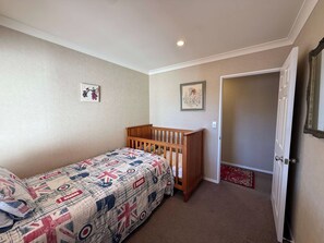 A room with a single bed, a wooden crib, a door, and a small rug. - Mooma's - Single Level, Covered Patio, Sleeps 8 (Rotorua)