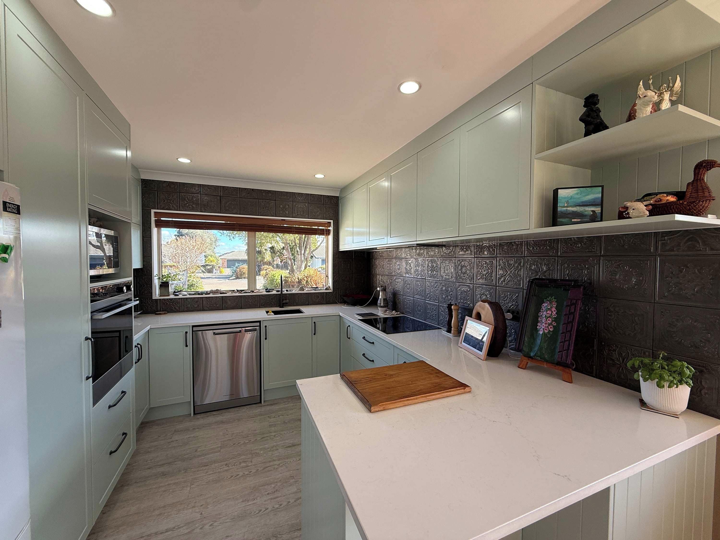 A modern kitchen with light-colored cabinets, a stainless steel dishwasher, and a window with a view of the outdoors.