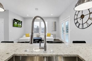 A modern kitchen with a stainless steel sink, white countertops, and a large wall clock. - 4BR, 3.5 Baths · Spa Tub · Near Downtown Columbus (Columbus)