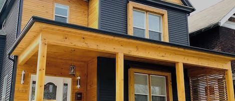 Una casa de dos pisos con fachada de madera, un porche cubierto y un techo negro.