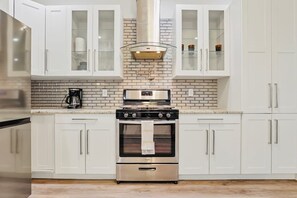 A kitchen with white cabinets, a stainless steel stove, and a brick backsplash. - 4BR, 3.5 Baths · Spa Tub · Near Downtown Columbus (Columbus)