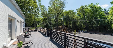Eine Holzterrasse mit Gartenmöbeln, Geländer und Blick ins bewaldete Gebiet.
